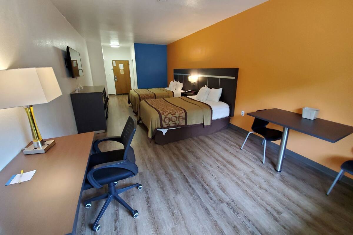 Una habitación de hotel con cama, escritorio, silla y televisor en la pared.