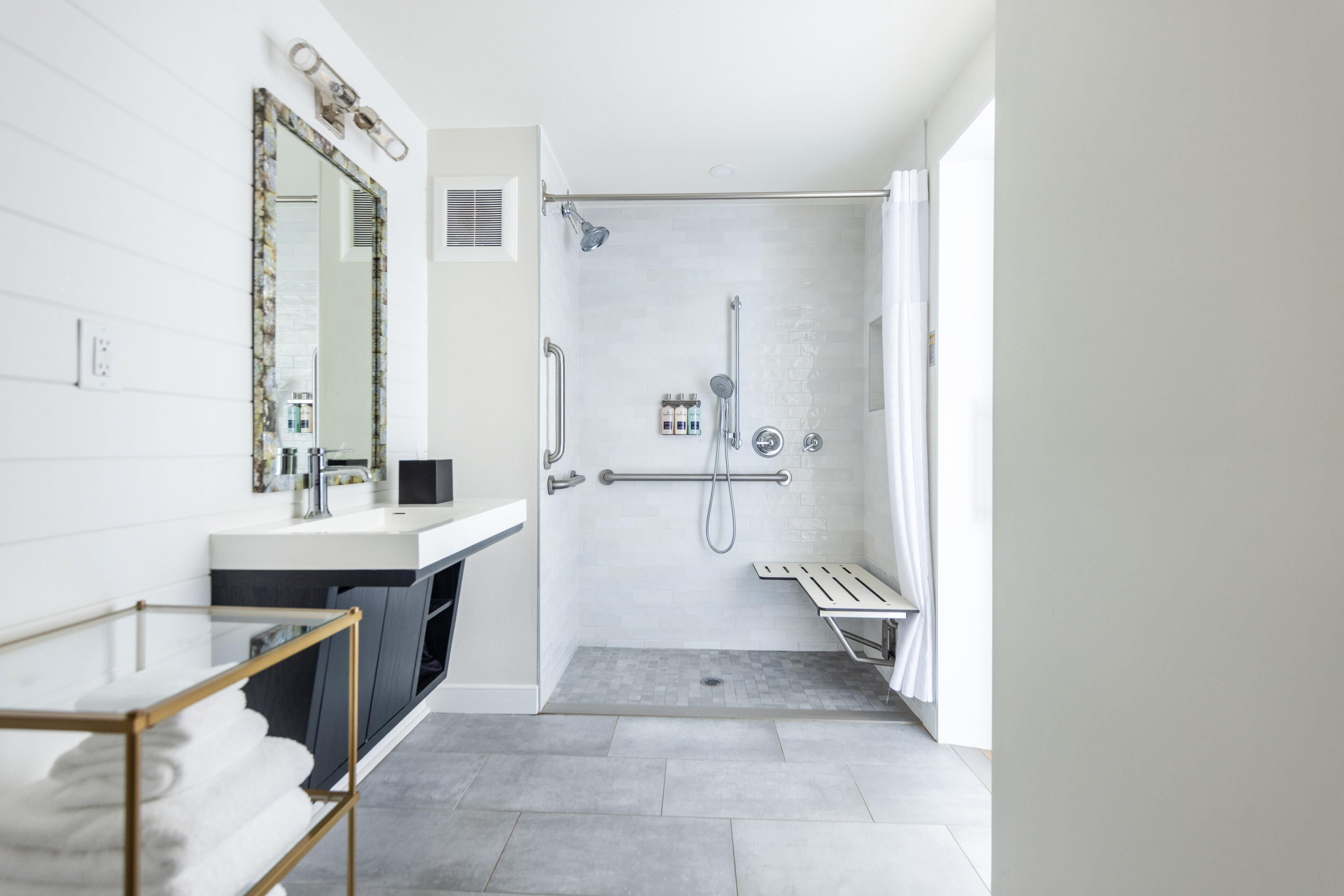 Une salle de bain moderne avec une douche, un meuble-lavabo avec un miroir et une table en verre sur laquelle sont posées des serviettes.