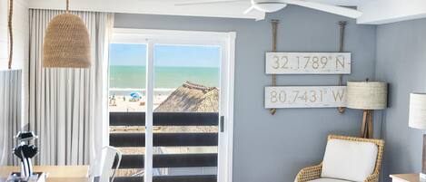A room with a beach view, a ceiling fan, a wicker chair, and a large window.