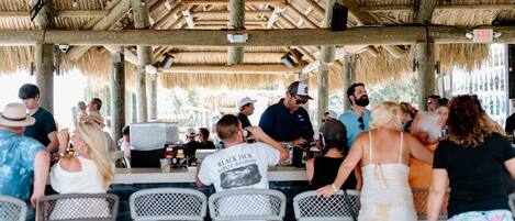 A covered outdoor seating area with metal chairs and a thatched roof.