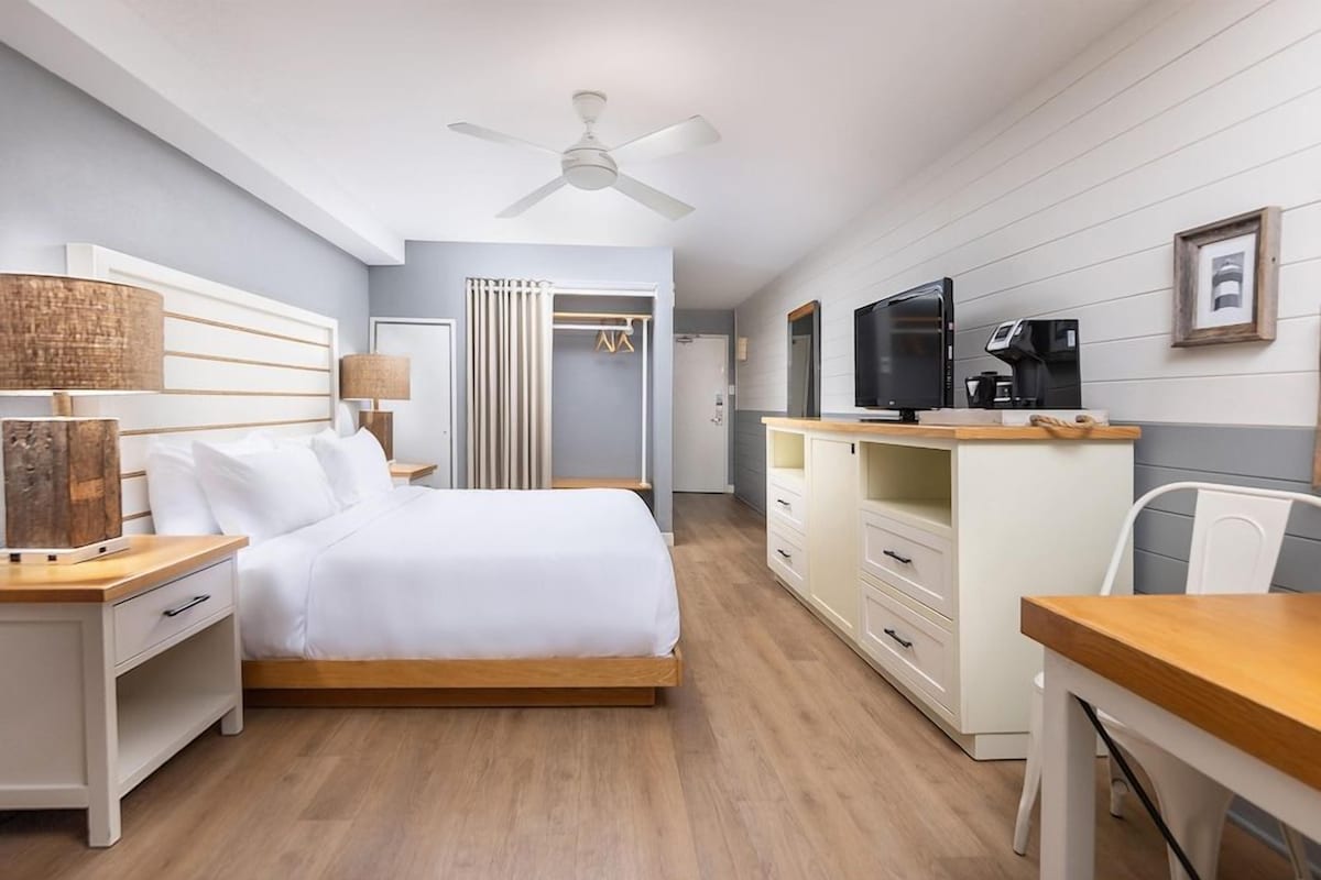 A bedroom with a bed, bedside tables, a desk, a chair, a television, and a wardrobe.