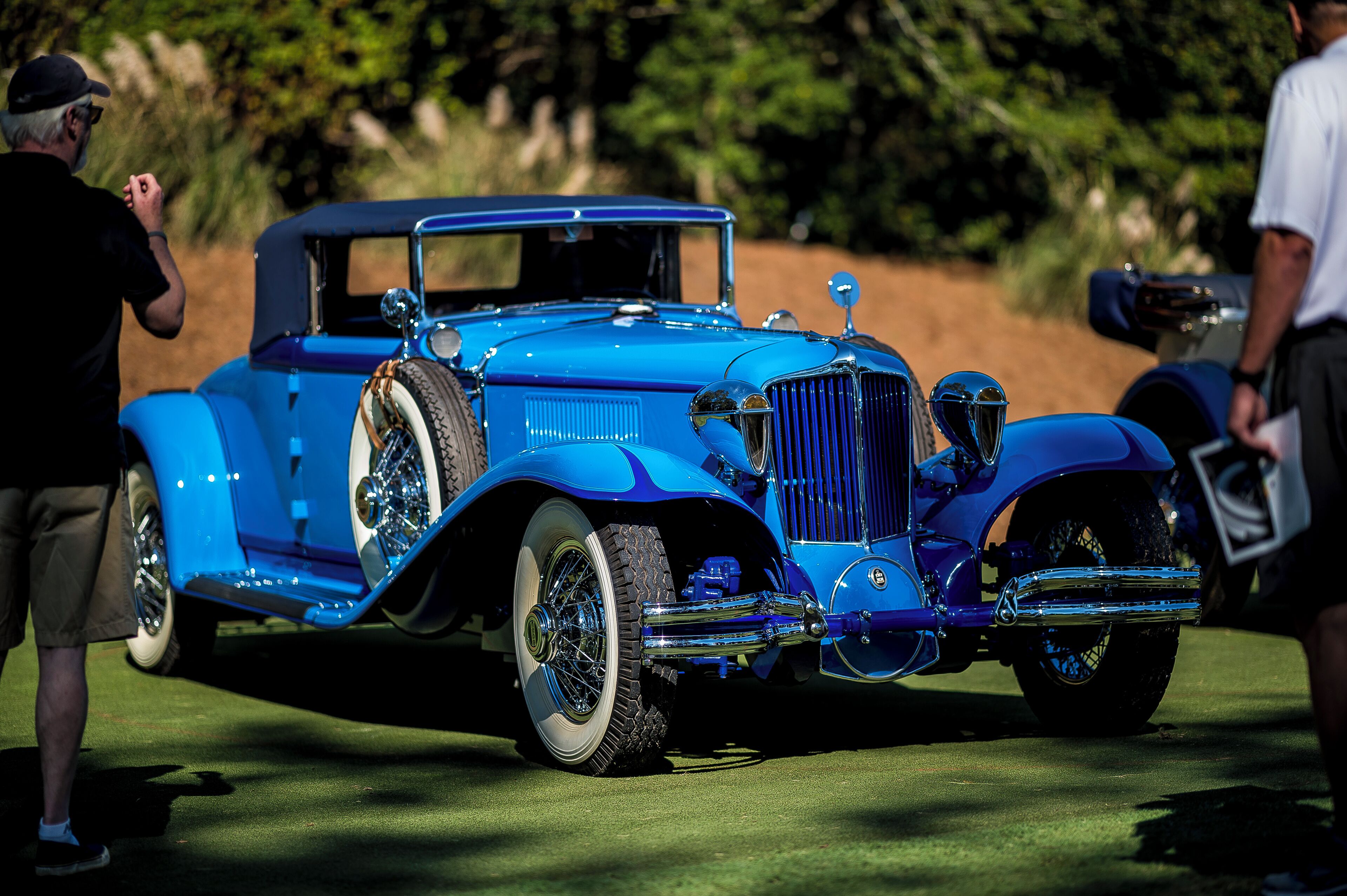 A vintage blue car with chrome details parked on a grassy area.