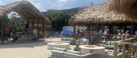 A beachside area with thatched-roof structures, outdoor seating, and bicycles.