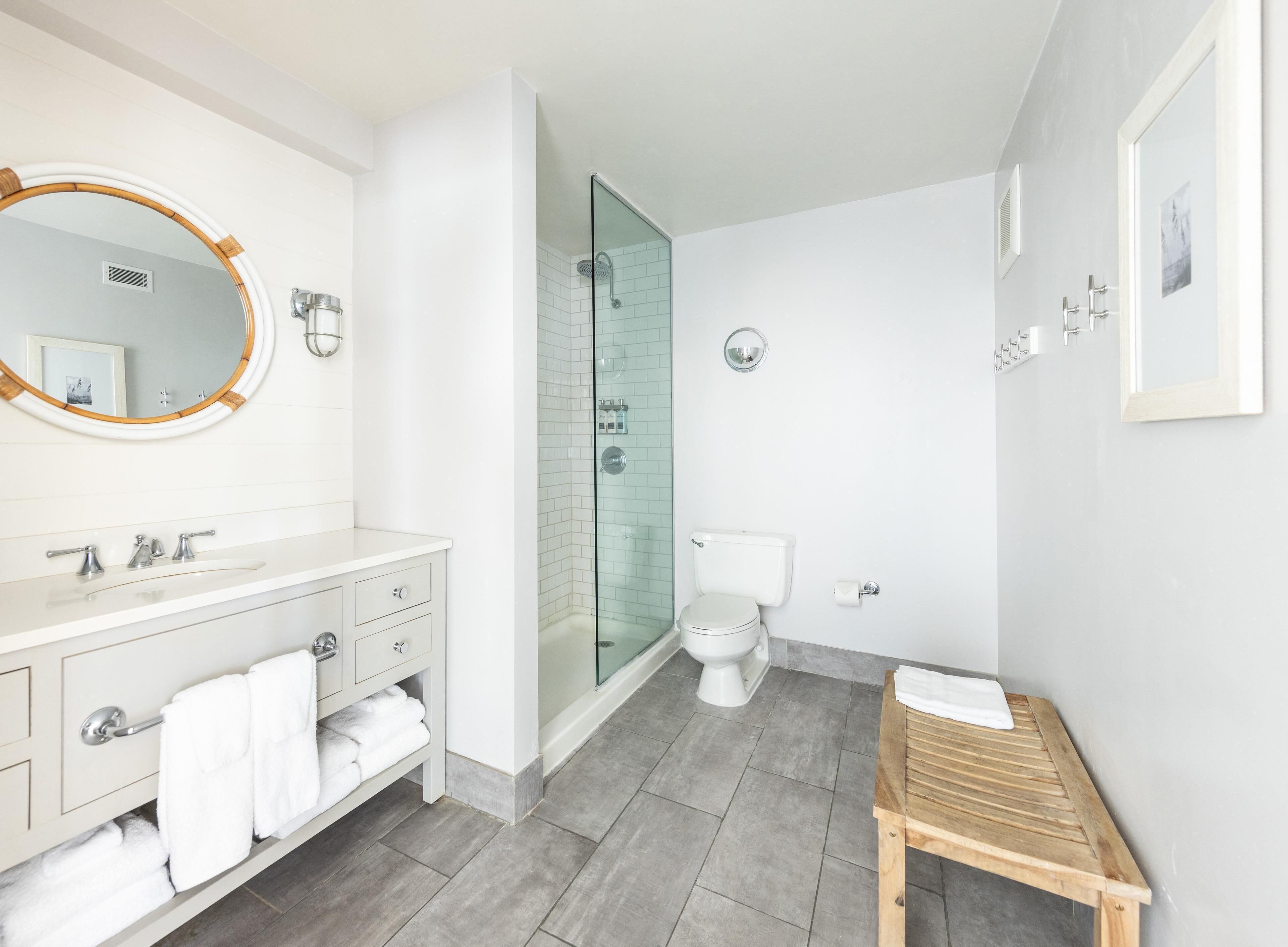 Et moderne badeværelse med vaskebord, toilet, bruser og en træbænk.