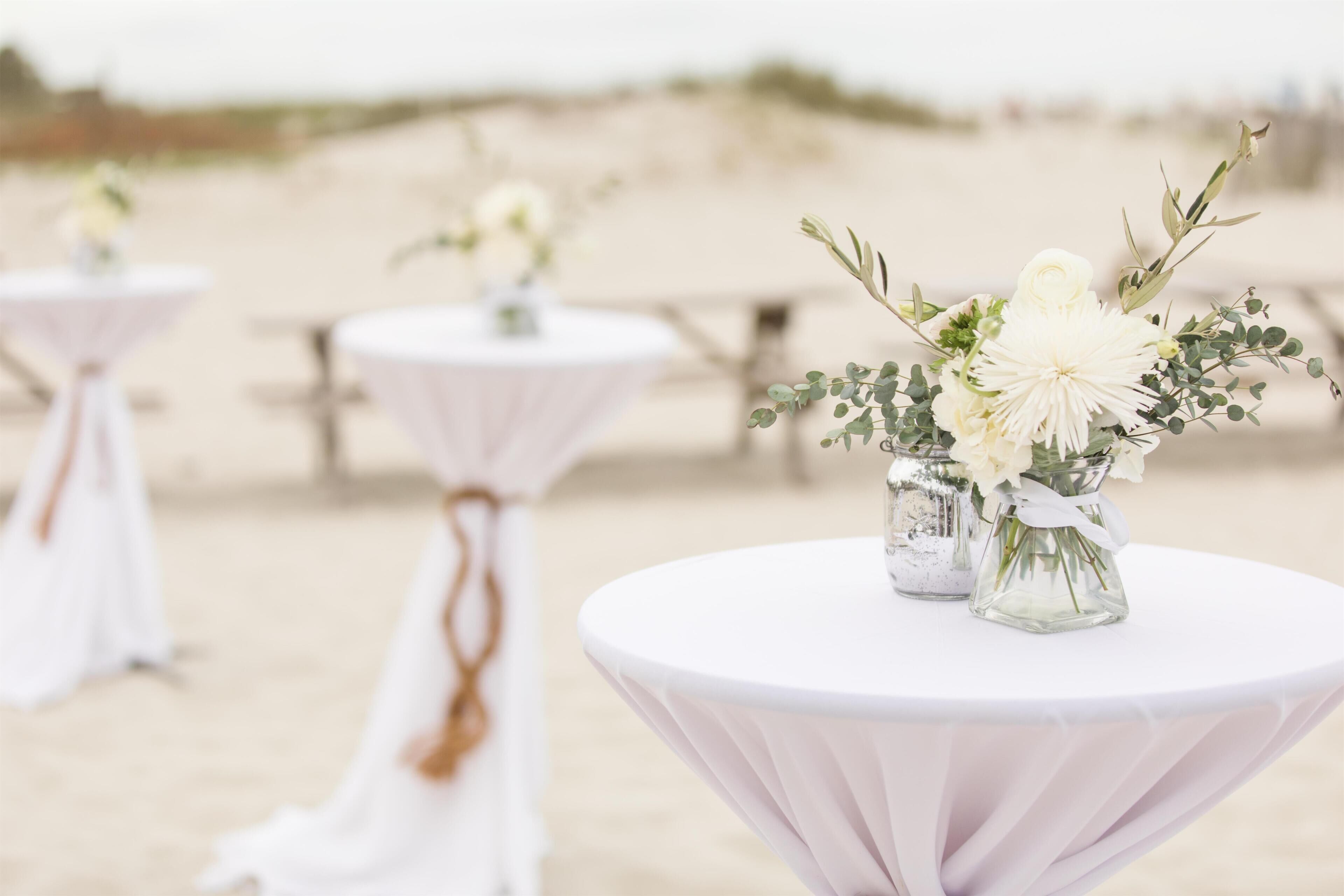 Round tables with white tablecloths and small vases with white flowers and greenery.