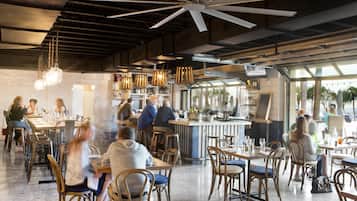 Un ristorante con soffitti alti, travi a vista e un'area bar. I tavoli sono disposti per la ristorazione e gli ospiti sono seduti.