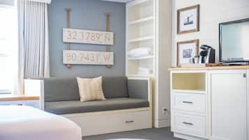 A hotel room with a grey sofa, a white cabinet, and a television. There are two framed signs on the wall displaying coordinates.