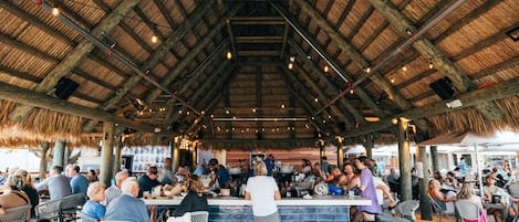 An outdoor dining area with a thatched roof, wooden beams, and a bar counter.