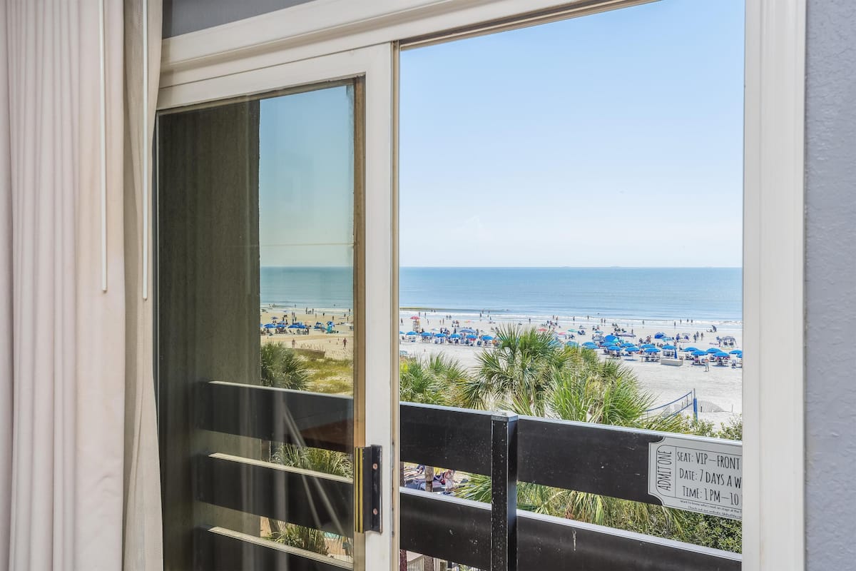 A view from a balcony with a beach in the background, a sign indicating VIP front seat admission, and a clear sky.