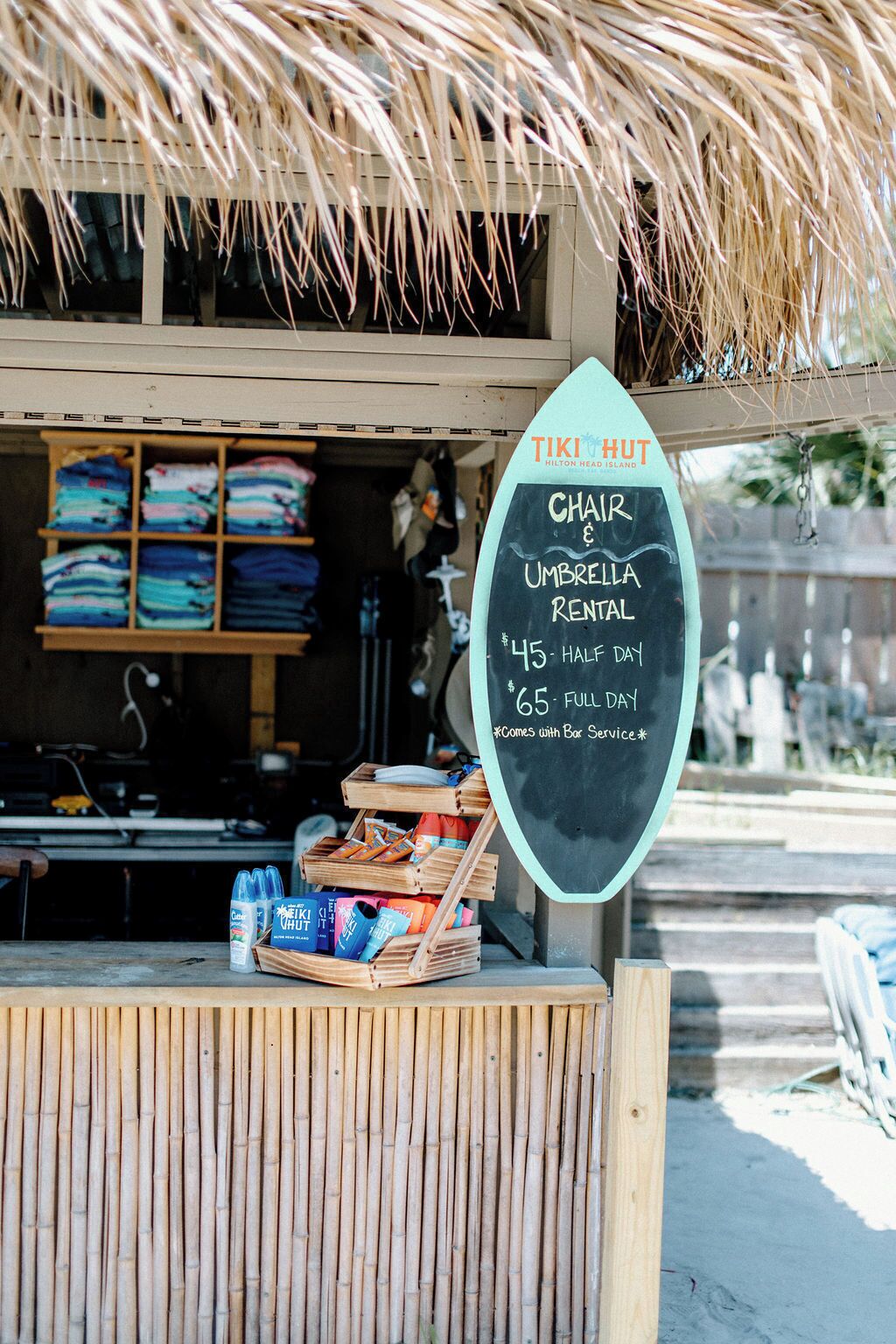 Um quiosque à beira-mar com um letreiro anunciando aluguel de cadeiras e guarda-sol por 45 dólares para meio dia e 65 dólares para o dia inteiro, incluindo serviço de bar.
