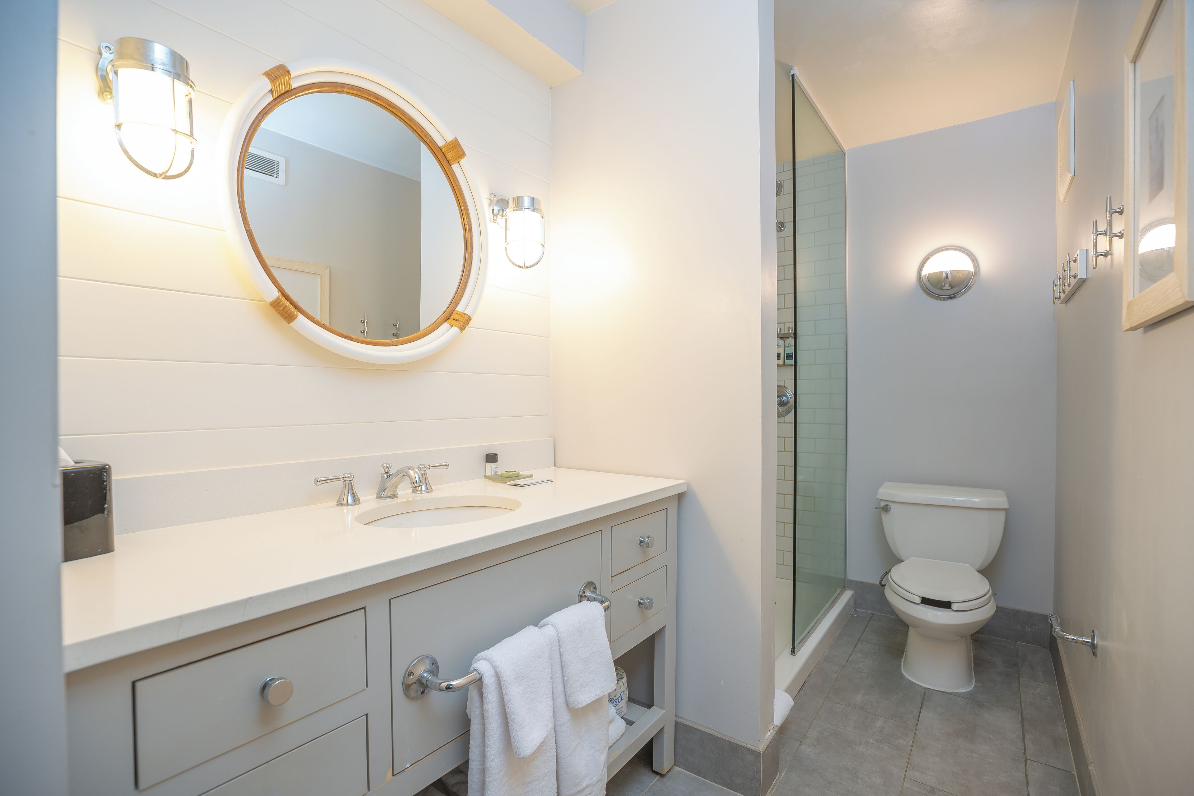 A modern bathroom with a white vanity, a round mirror, and a toilet.