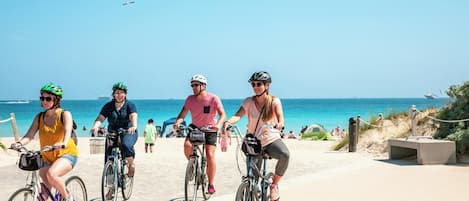 Three people riding bicycles on a paved path by the beach.