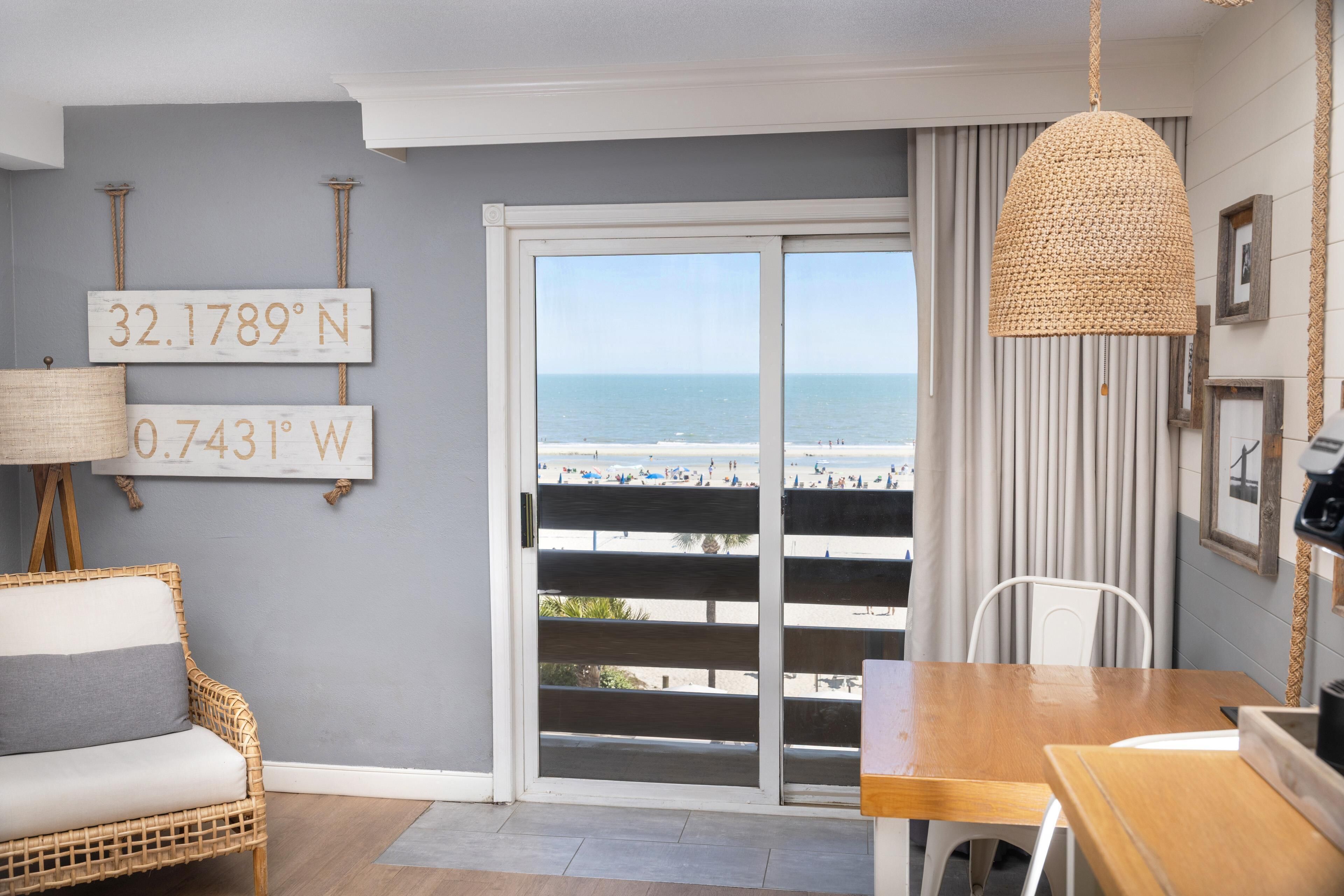 A room with a wicker sofa, a wooden table, a hanging woven light fixture, and a view of the beach through a sliding door.