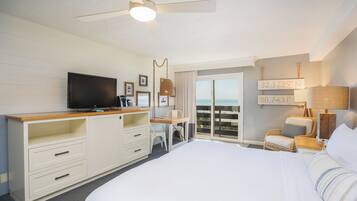 Habitación de hotel con cama, escritorio, televisión, ventilador de techo y vista al océano.