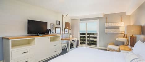 Habitación de hotel con cama, escritorio, televisión, ventilador de techo y vista al océano.