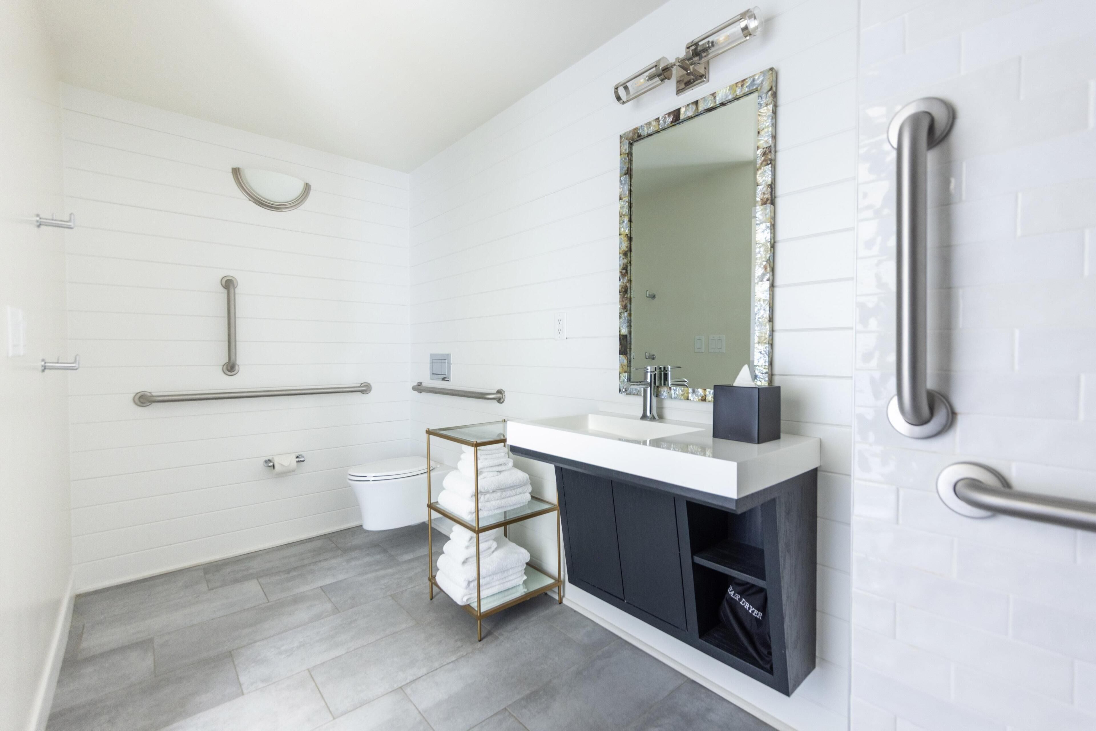 A modern bathroom with white tiled walls, a large mirror, a sink, and a towel rack.