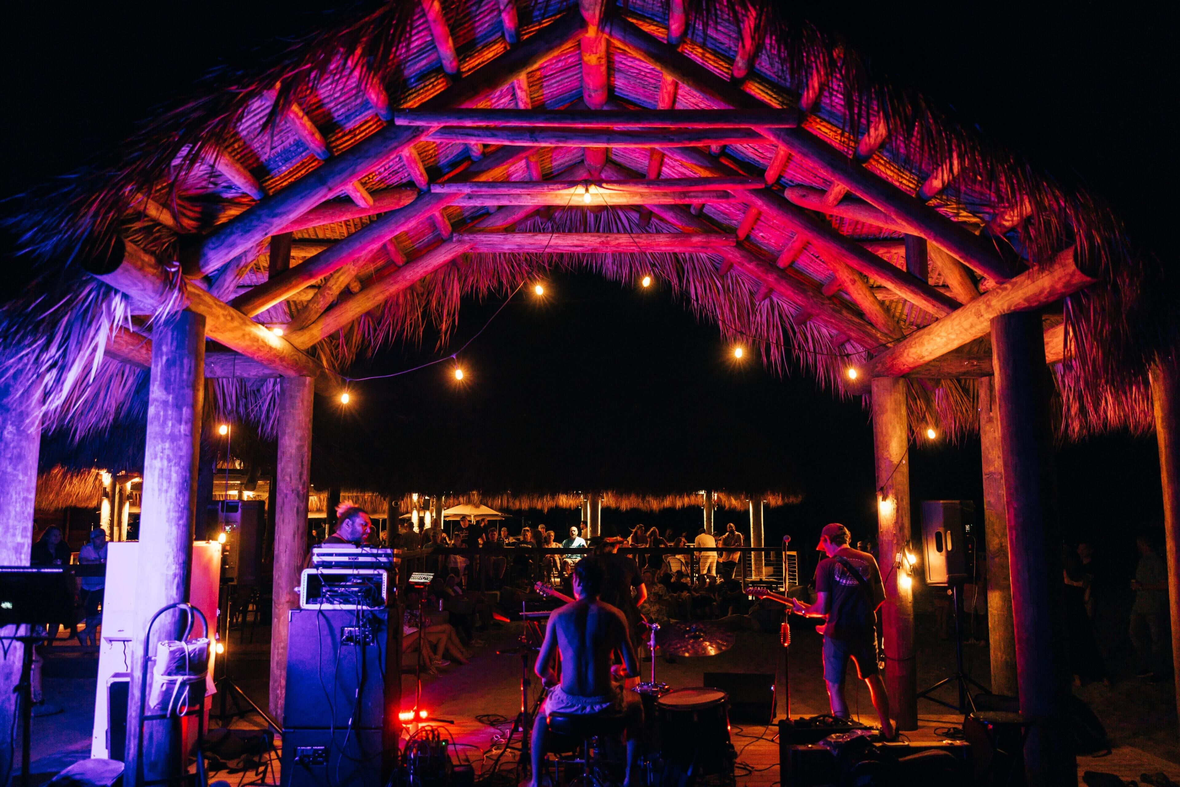 An outdoor venue with a thatched roof structure, musical equipment, and a stage for performances.