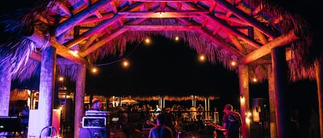 An outdoor venue with a thatched roof structure, musical equipment, and a stage for performances.