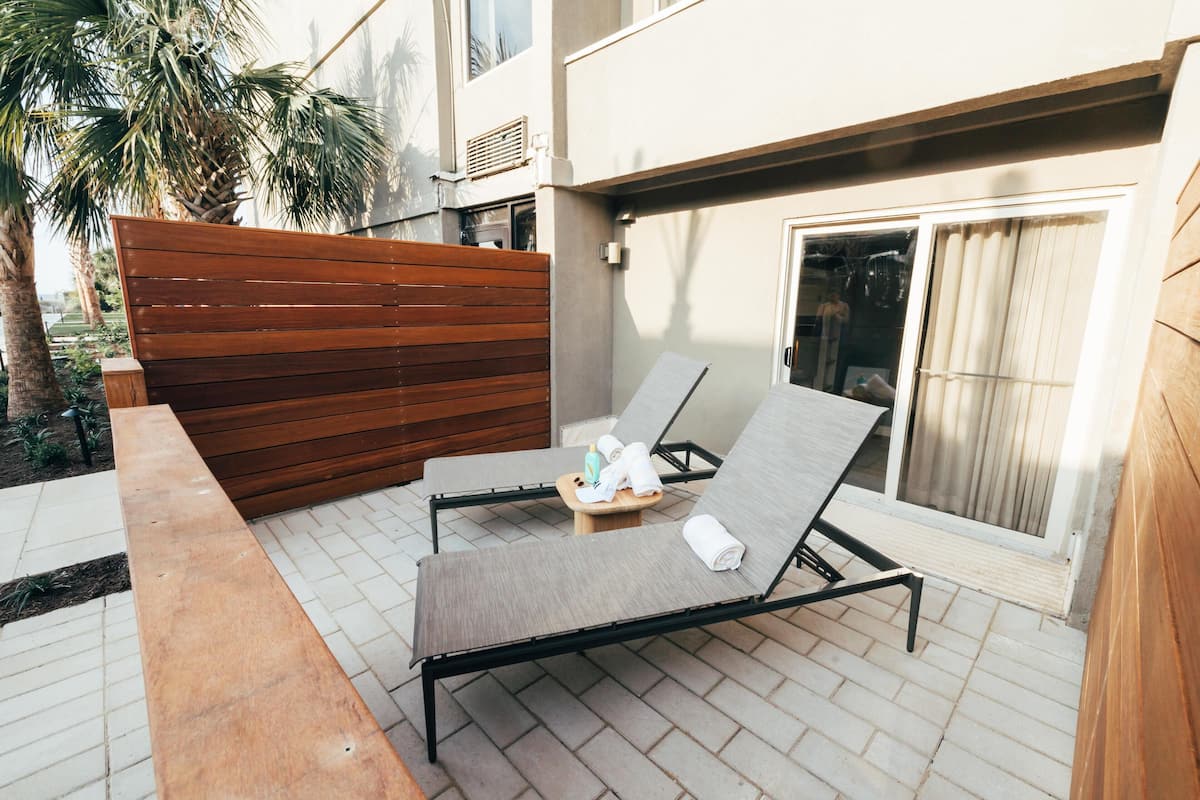 A patio with two lounge chairs, a wooden bench, and a small table with towels and a bottle.