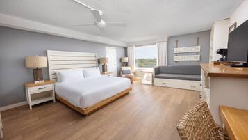 A modern hotel room with a bed, bedside tables, a desk, a chair, a TV, and a view of the outdoors.