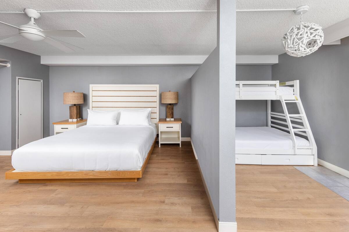 A bedroom with a bed, bedside tables, a ceiling fan, a bunk bed, and a hanging light fixture.