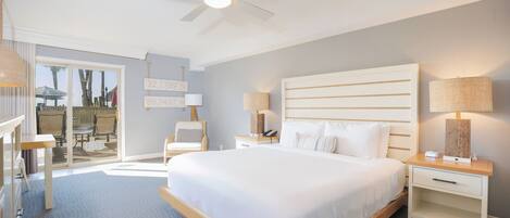 Una habitación de hotel moderna con una cama grande, un ventilador de techo y vistas del patio exterior.