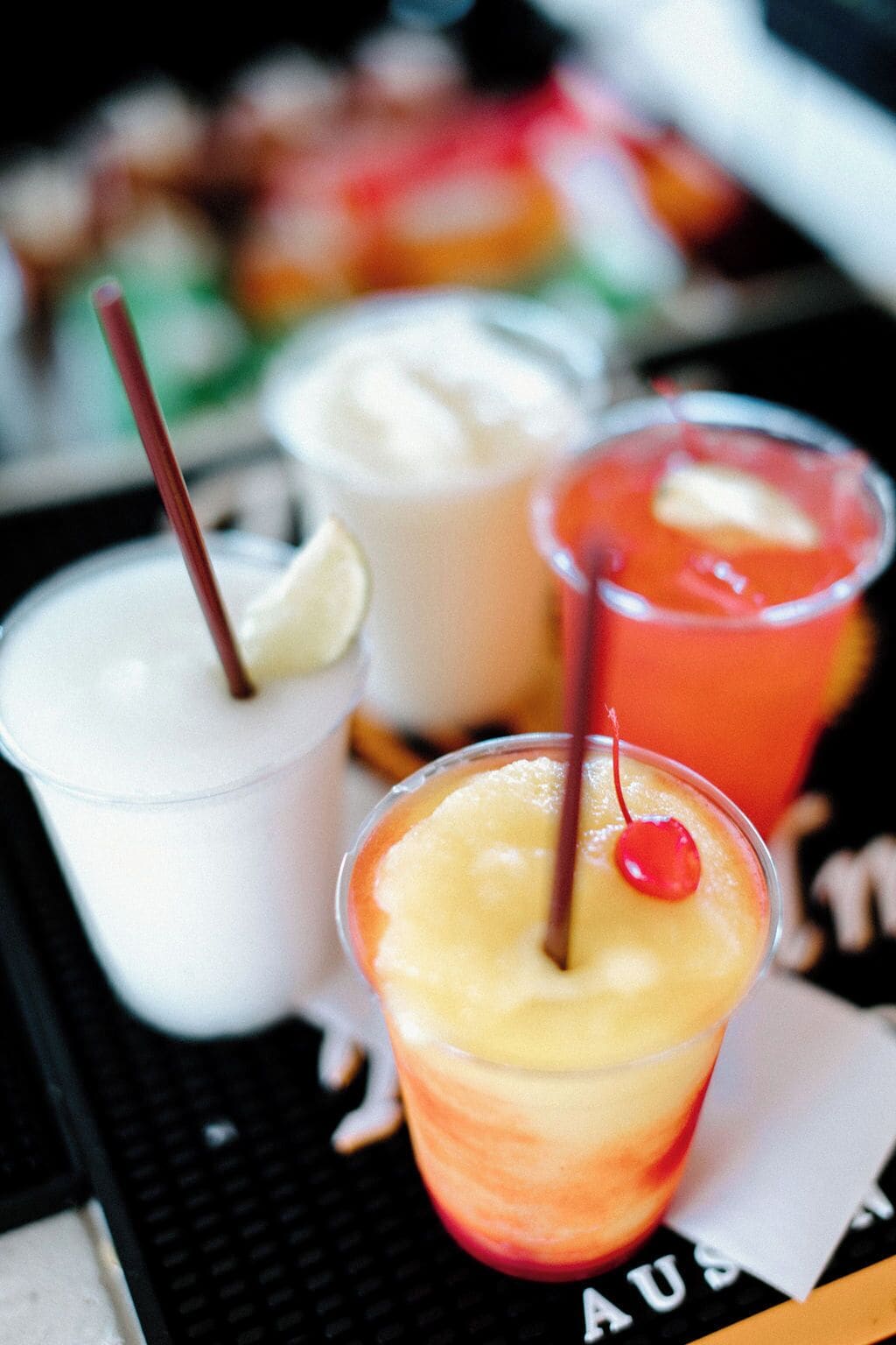 Three drinks in clear glasses with straws, one with a cherry on top.