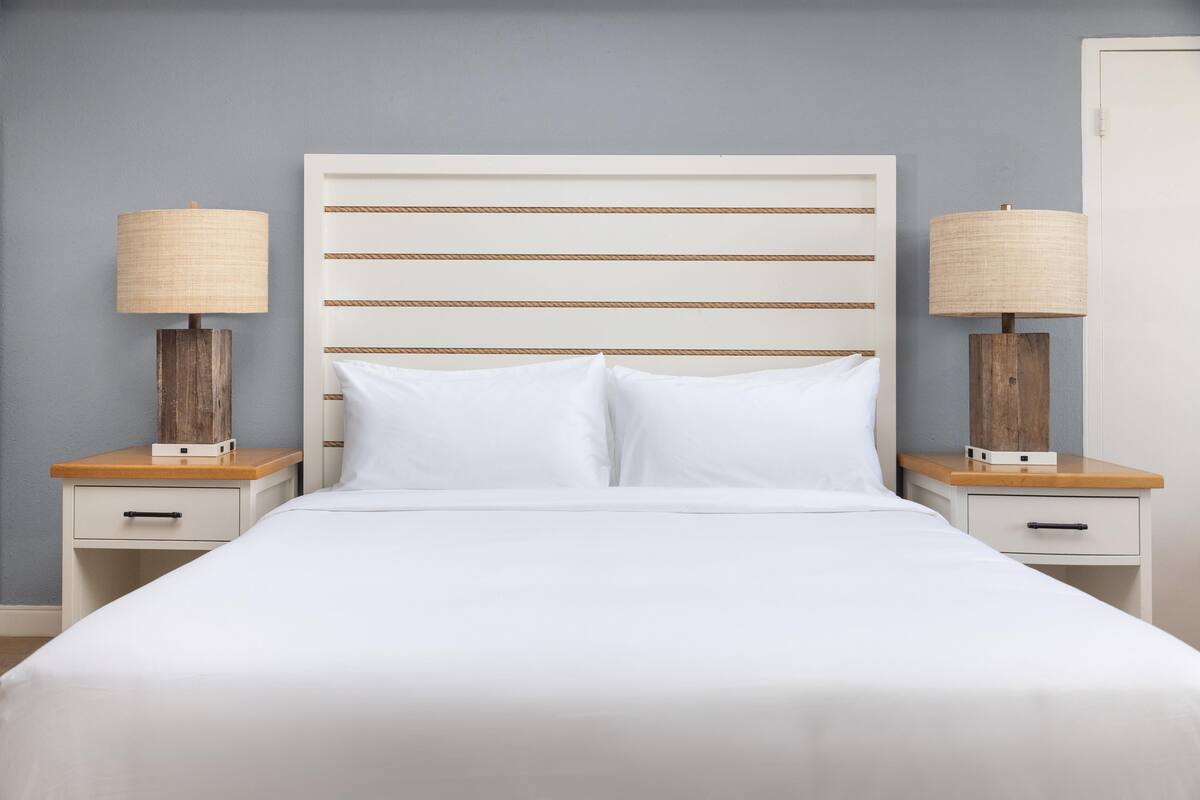 A bed with white bedding, a wooden headboard, and two bedside tables with lamps.