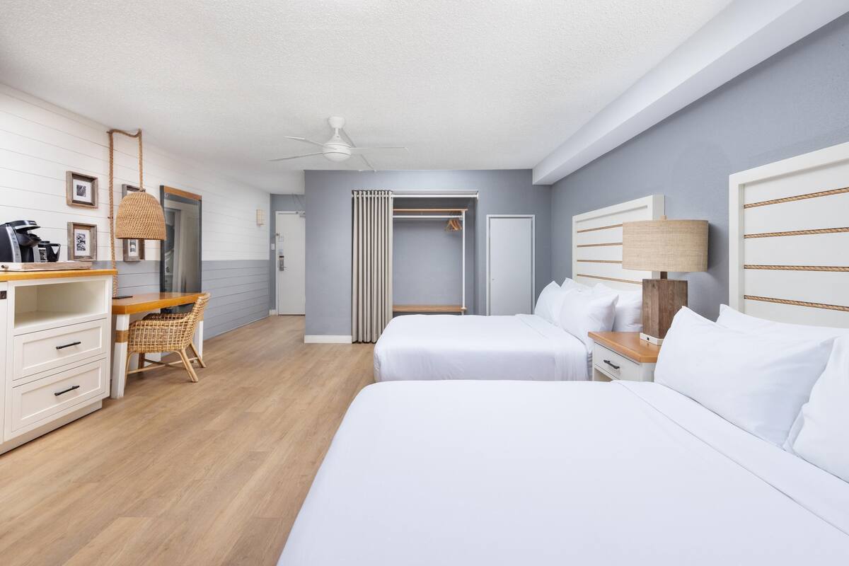 Een hotelkamer met twee bedden, een bureau met stoel, een kledingkast en een plafondventilator.