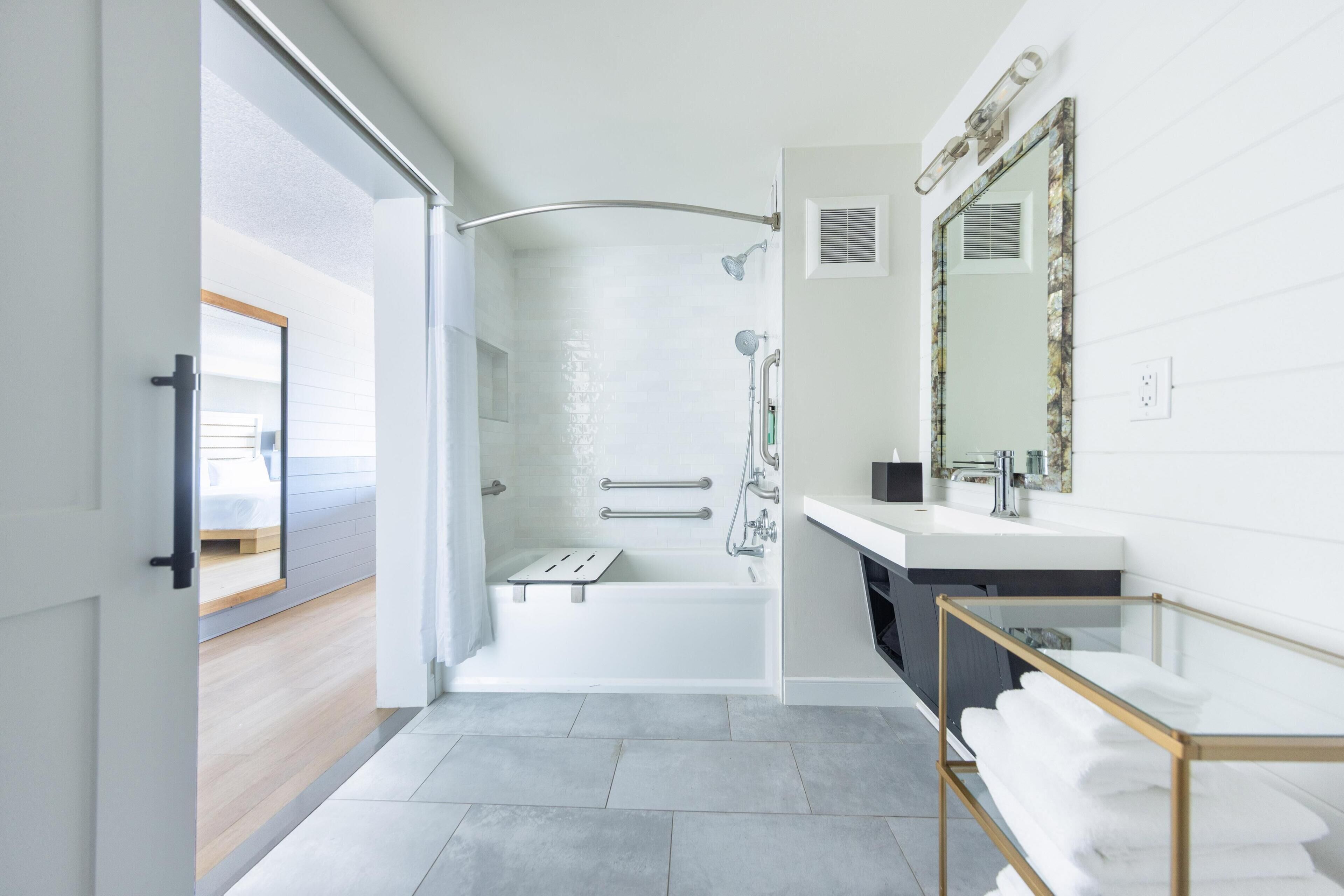 A modern bathroom with a shower, a bathtub, a vanity with a mirror, and a glass-topped sink.
