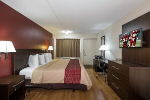 Une chambre d’hôtel comprenant un lit, des tables de chevet, un bureau, une chaise, une armoire, un téléviseur et une fenêtre avec des rideaux.