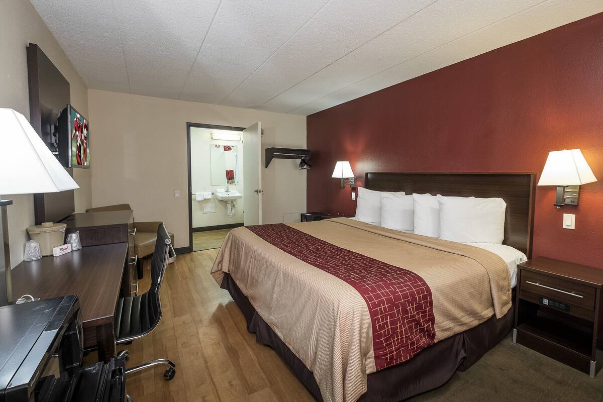 A hotel room with a large bed, two bedside lamps, a desk with a chair, and a small table.