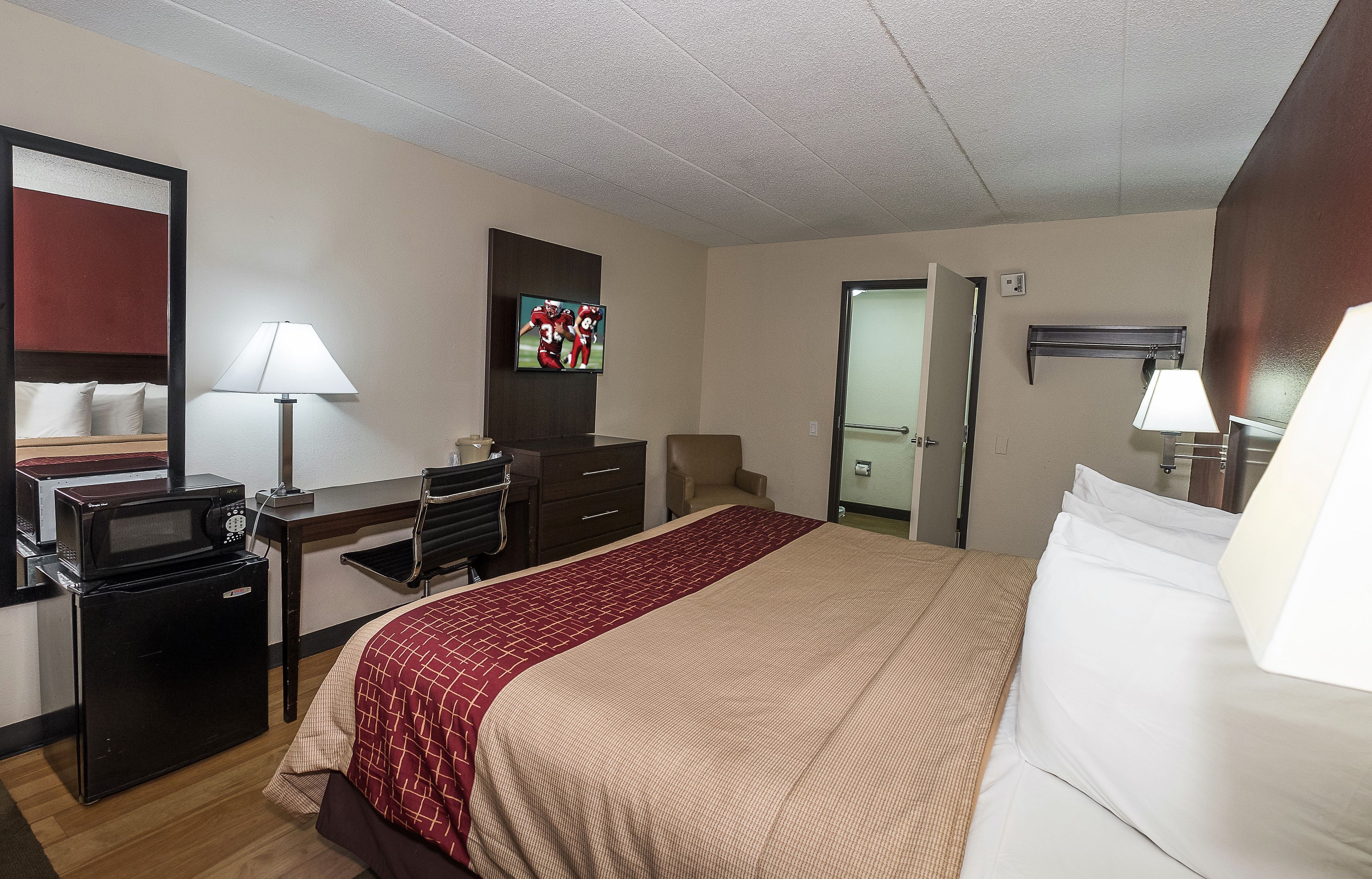 A hotel room with a bed, a desk with a computer, a television, and a mirror.