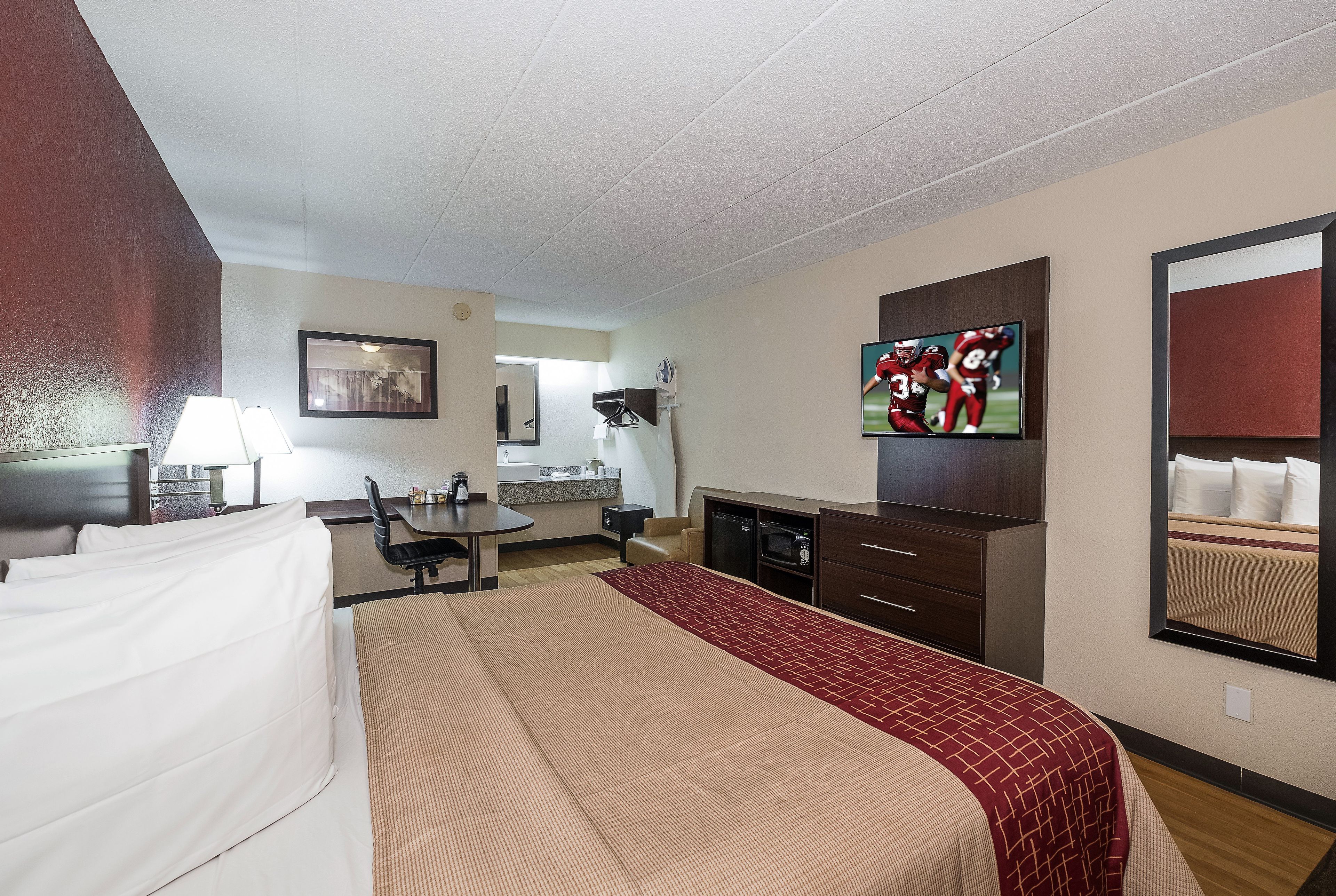 Habitación de hotel con cama, escritorio, televisión, espejo y kitchenette.