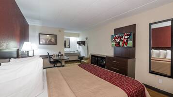 Habitación de hotel con cama, escritorio, televisión, espejo y kitchenette.