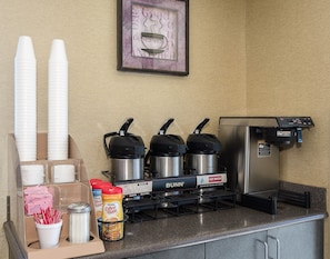 A coffee station with a Bunn coffee machine, disposable cups, and various coffee pods.