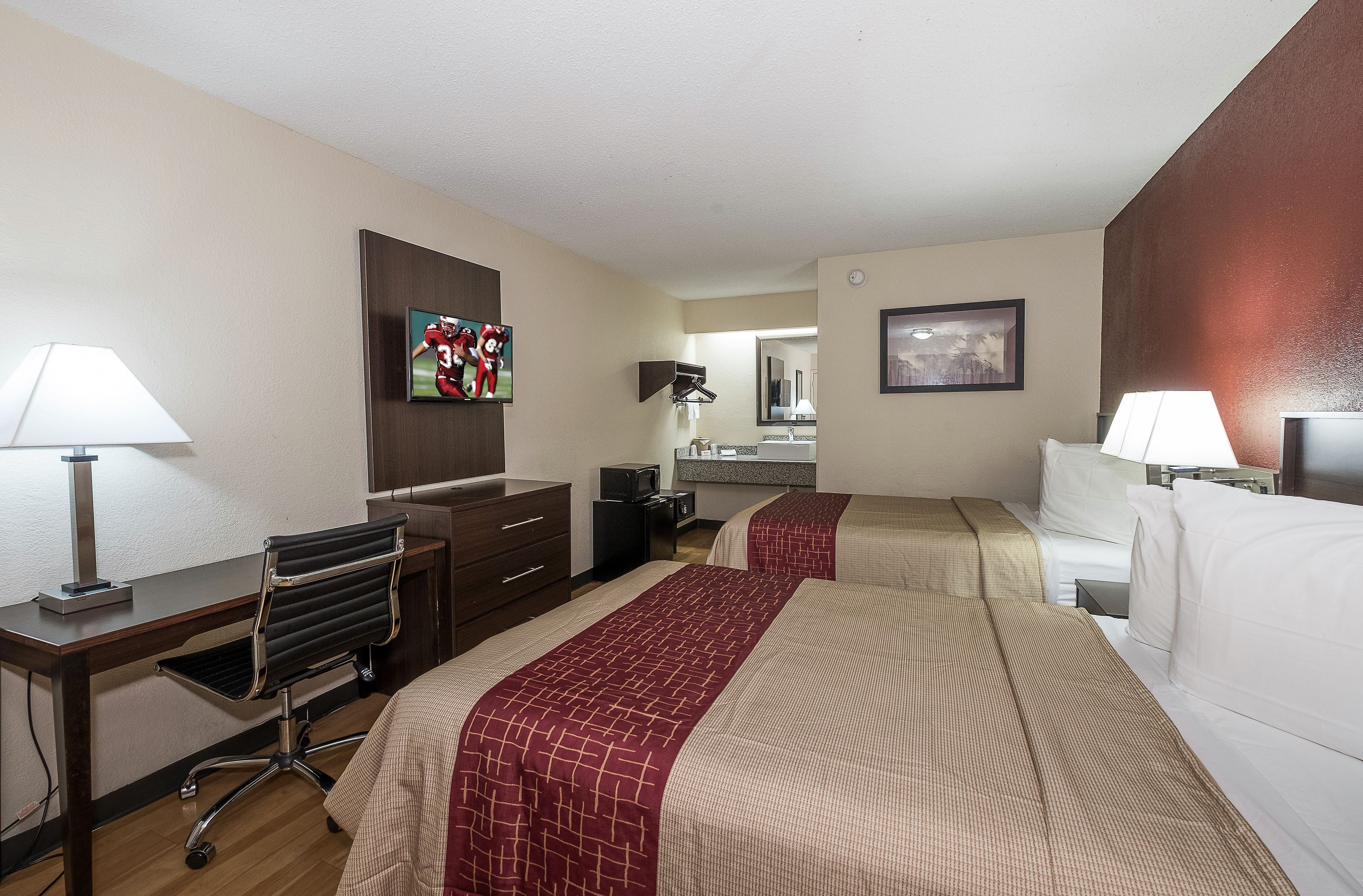Habitación de hotel con dos camas, un escritorio, una silla, un televisor, un espejo y un baño.