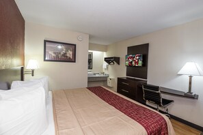 A hotel room with a bed, a desk, a chair, a television, and a bathroom visible through an open door. - Red Roof Inn Columbus East - Reynoldsburg (Columbus)