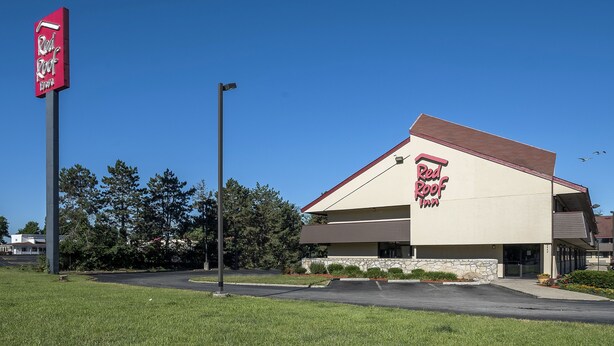 A Red Roof Inn with a clear sky, a parking lot, and surrounding trees. - Red Roof Inn Columbus East - Reynoldsburg (Columbus)