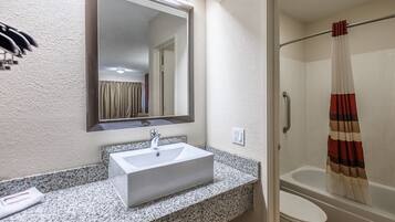 Un baño con lavamanos, espejo, cortina de ducha e inodoro.