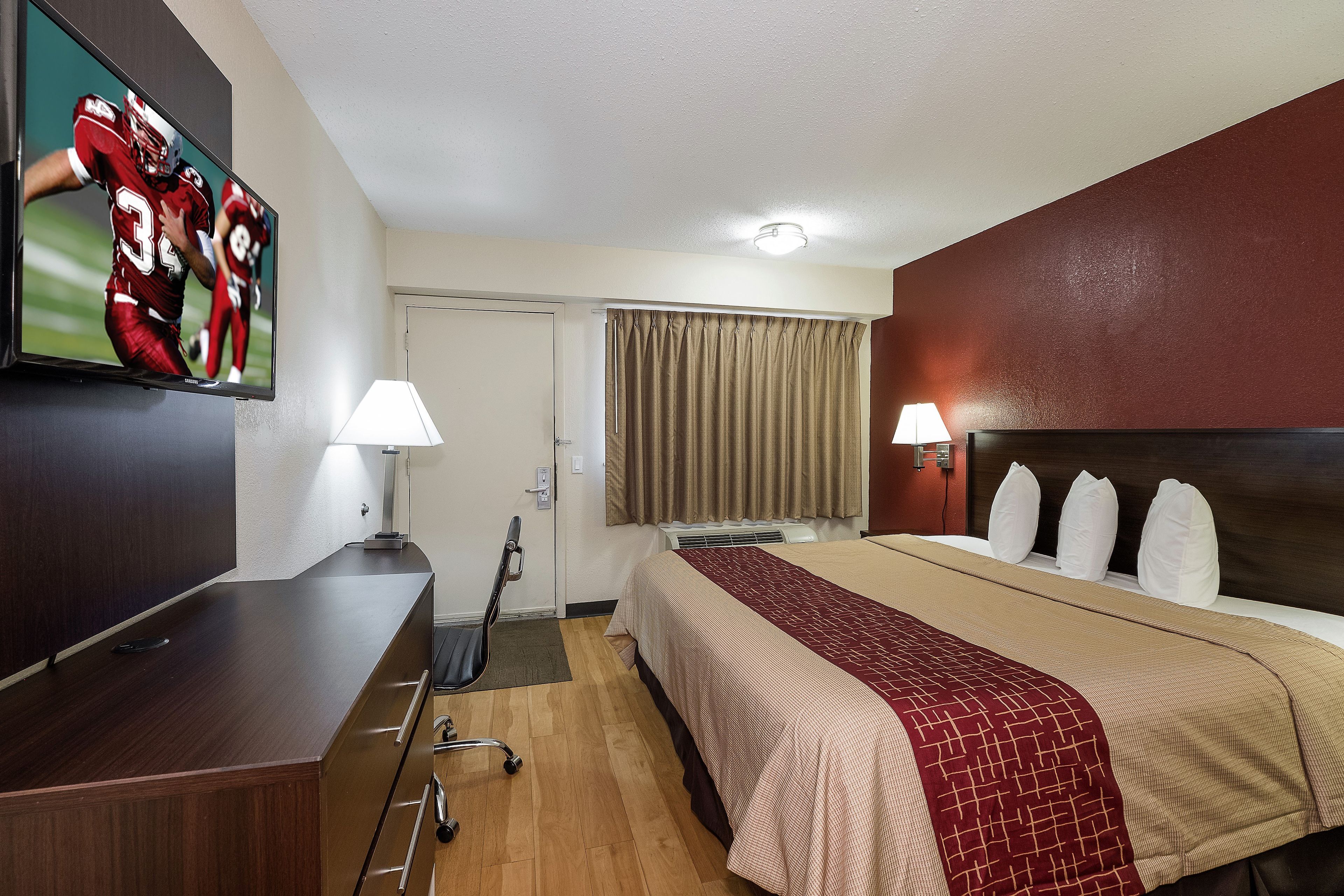 A hotel room with a bed, a desk, a television, and a window with curtains.