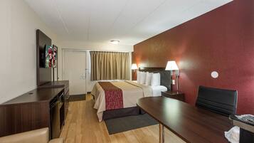 A hotel room with a bed, desk, chair, TV, and a red accent wall.