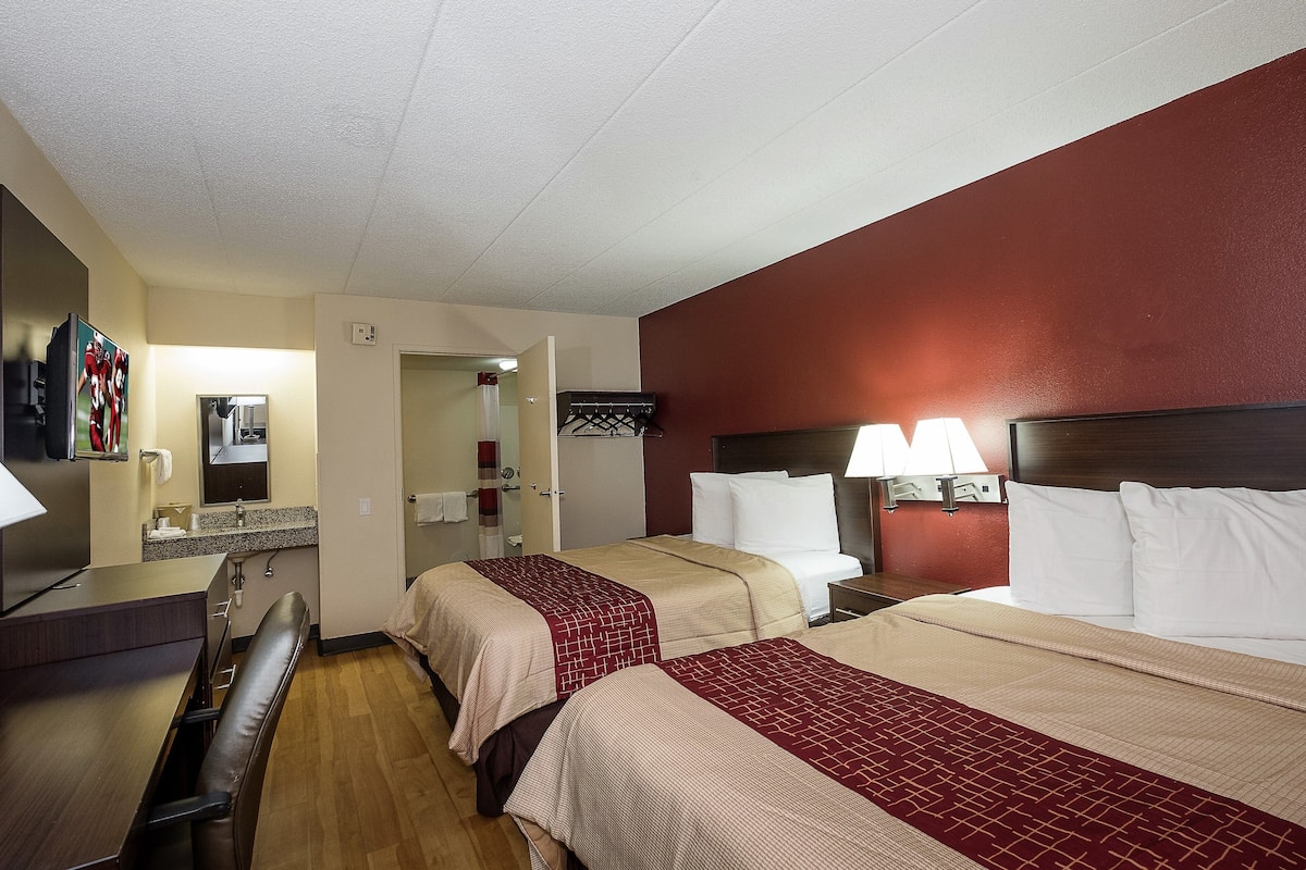 A hotel room with two beds, a desk, a chair, a mirror, a sink, and a wardrobe.