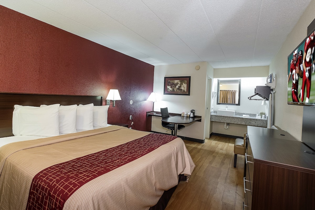 A hotel room with a large bed, a desk with a chair, a small bathroom, and a TV.