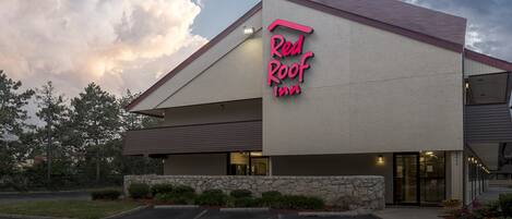Ett Red Roof Inn-hotell med en fasad av sten, ett sluttande tak och en parkeringsplats.