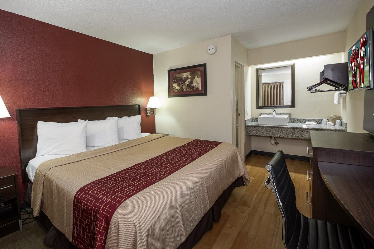 A hotel room with a bed, bedside lamps, a desk, a mirror, and a bathroom with a sink and towel rack.