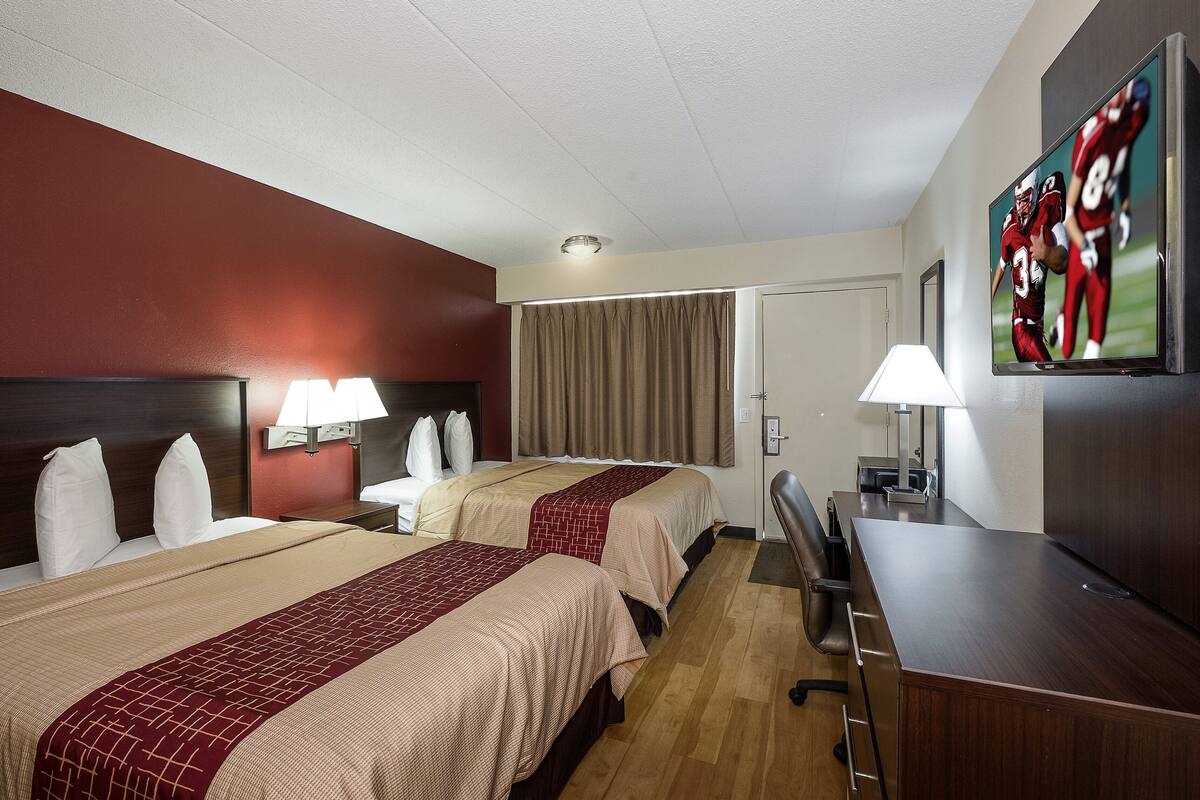 Une chambre d’hôtel avec deux lits, un bureau, une télévision et une porte.