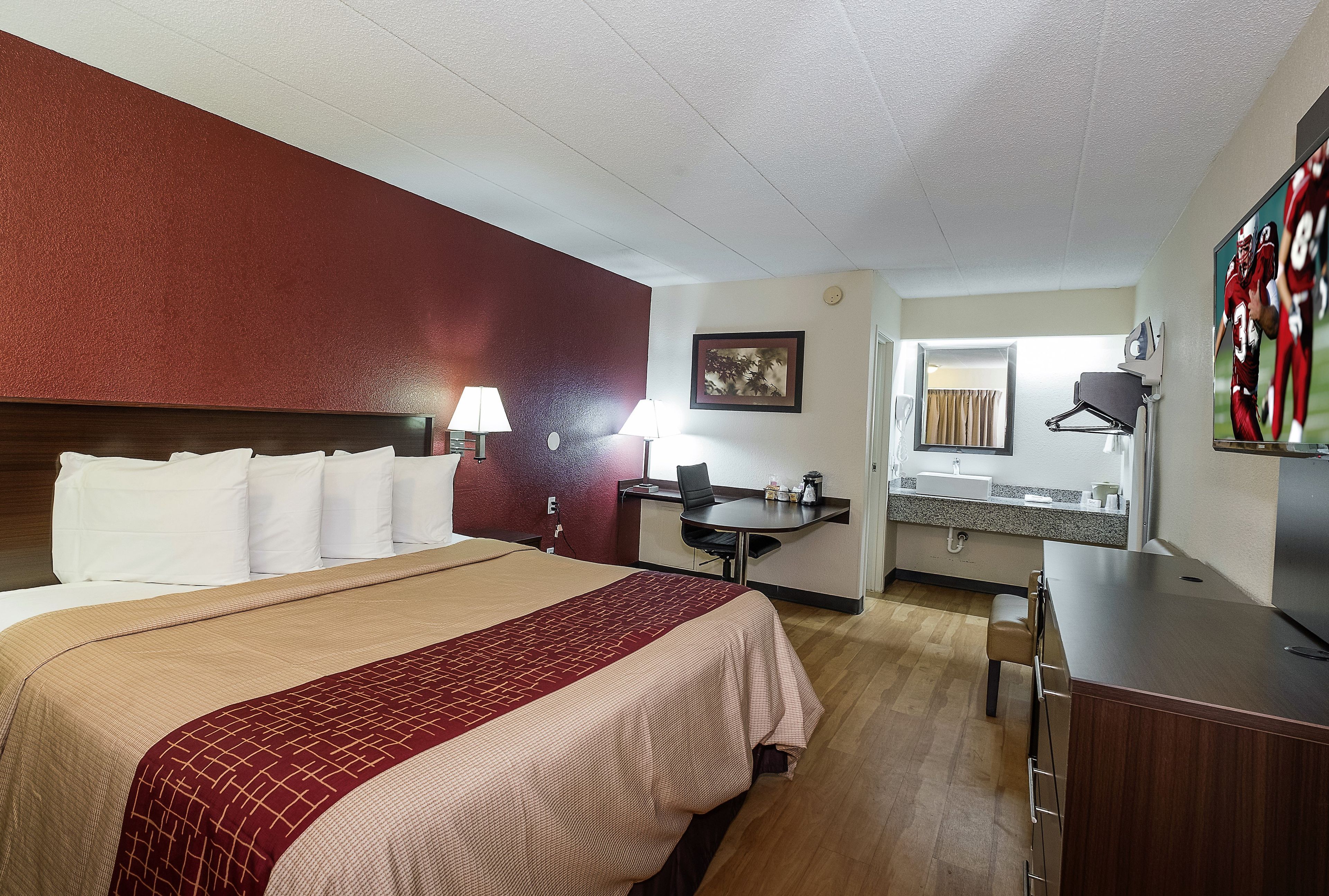 Ett hotellrum med en säng, ett nattduksbord, en lampa och ett litet skrivbord med en stol.