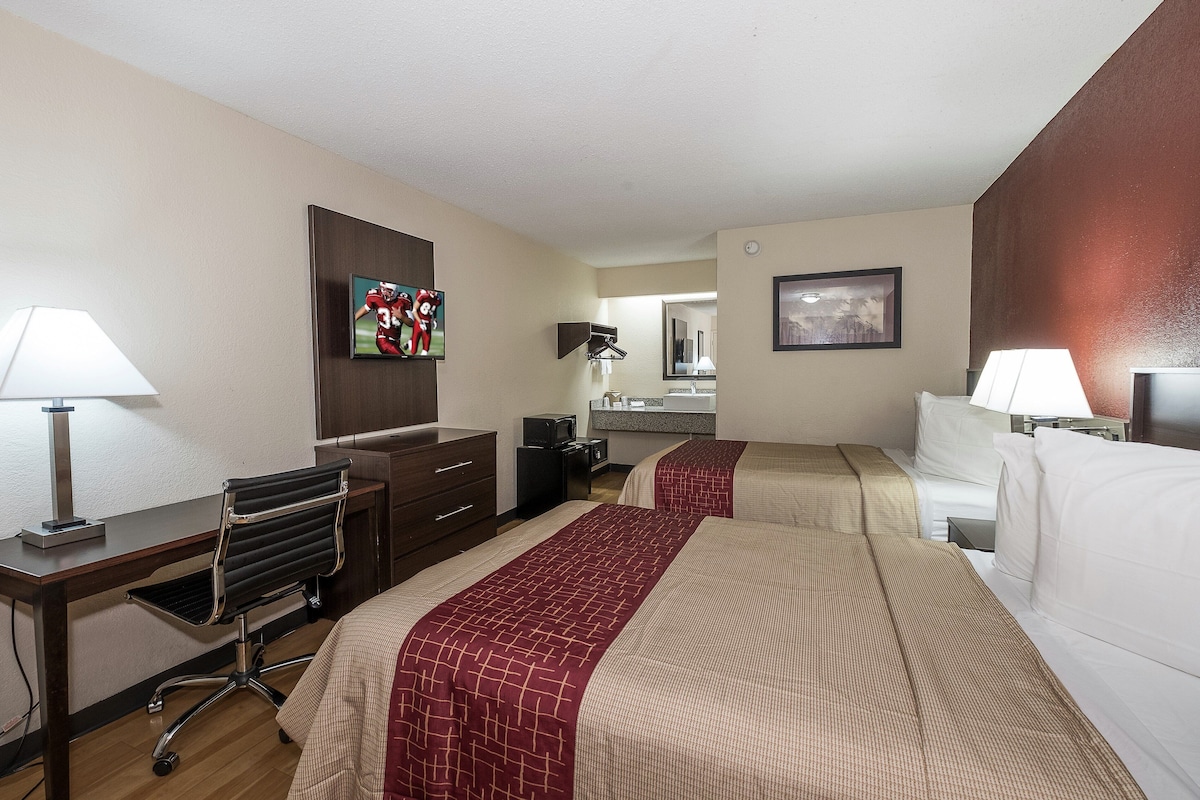 Habitación de hotel con dos camas, un escritorio, una silla, un aparador, un espejo y un televisor.