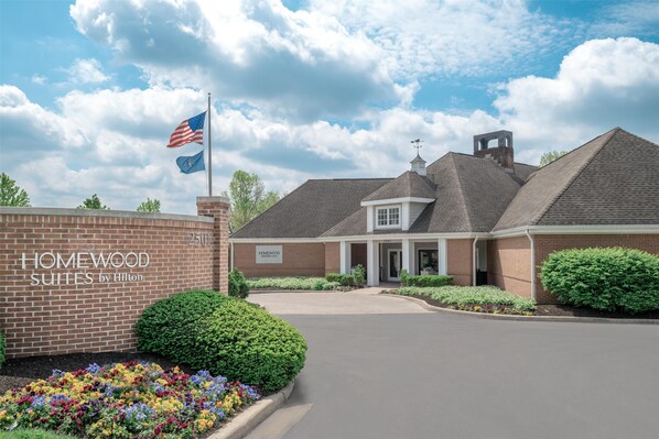 A hotel entrance with a brick facade, a flag, and a sign reading "Homewood Suites by Hilton."